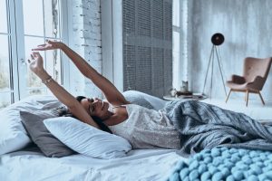 Attractive young woman smiling and stretching while lying on the bed at home